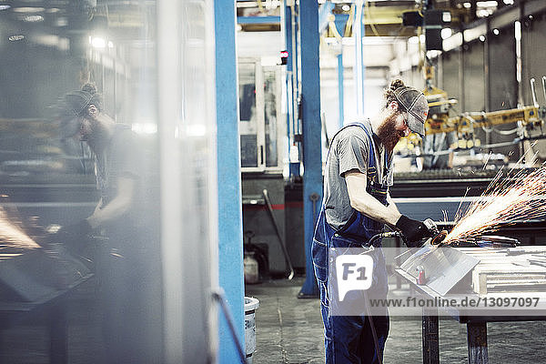 Worker wearing bib overalls while using welding machine in steel factory