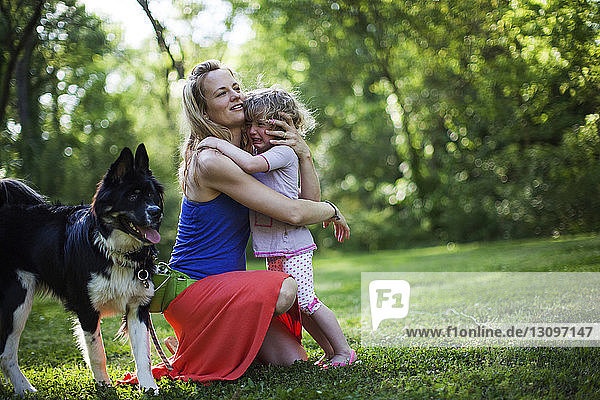 Mother embracing crying daughter by dog on field