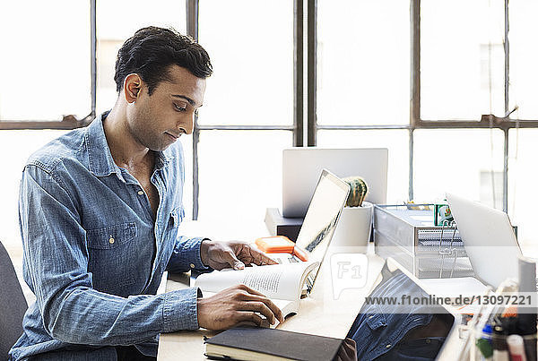 Selbstbewusster Geschäftsmann liest Buch am Schreibtisch im Büro