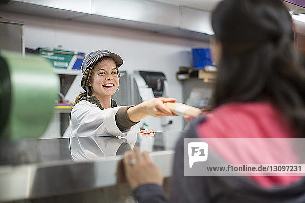Lächelnder Arbeiter übergibt Päckchen an Kunden im Supermarkt