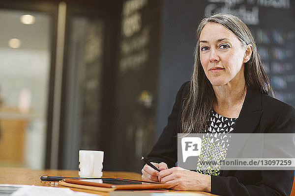 Porträt einer selbstbewussten Geschäftsfrau am Tisch sitzend mit Tablet-Computer im Büro
