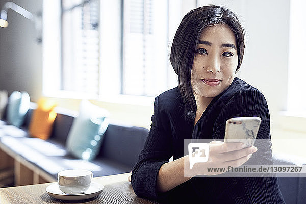 Portrait of happy businesswoman using smart phone while sitting in office cafeteria