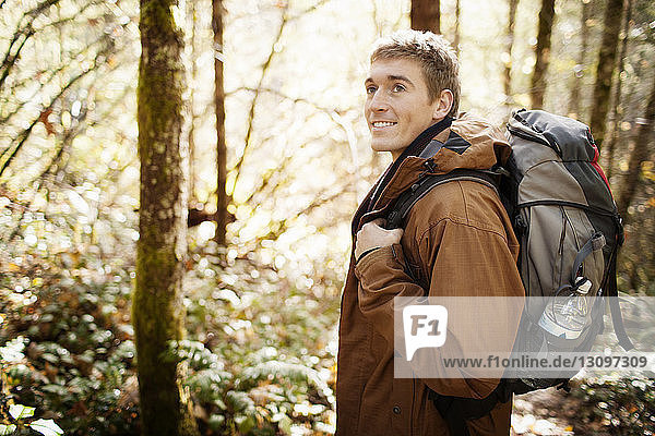 Man carrying backpack while looking away in forest