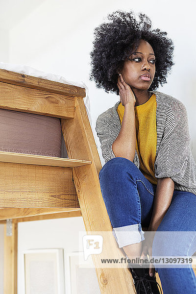 Woman looking away while sitting on ladder at home