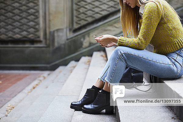 Low section of woman using phone while sitting on steps at park