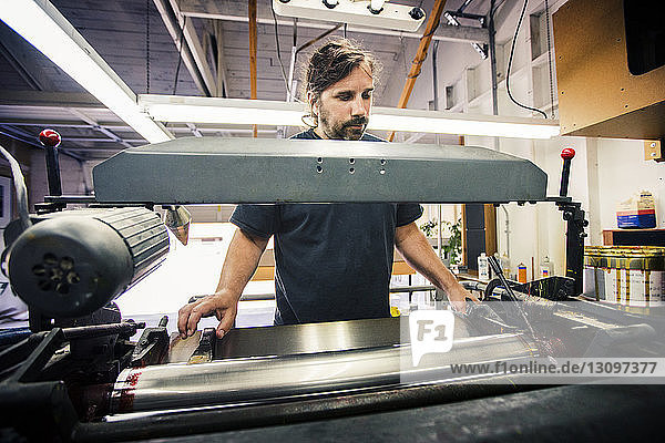 Männlicher Arbeiter benutzt Druckmaschine in der Werkstatt