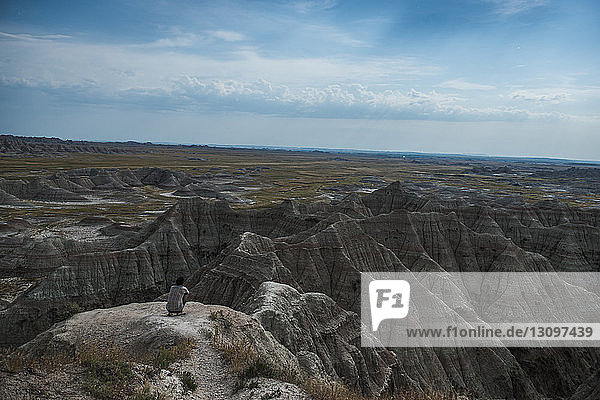 High angle view of hiker crouching on rocks at Badlands National Park against sky