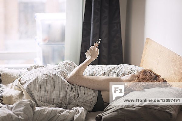 Frau benutzt Smartphone im Bett liegend