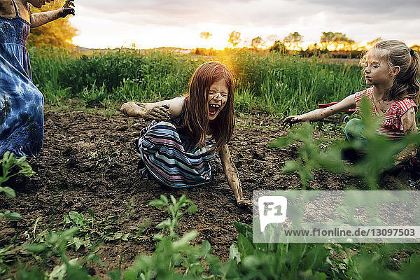 Girl with sisters shouting while crouching in mud