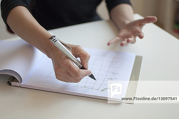 Cropped hand of businesswoman writing on book at desk in office