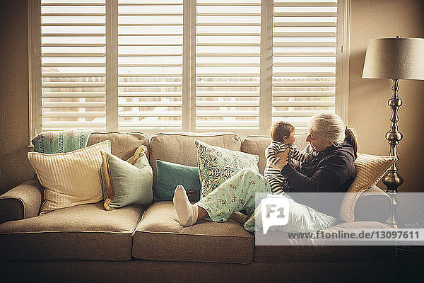 Grandmother playing with baby grandson on sofa against window
