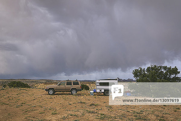 Car and travel trailer on field against cloudy sky