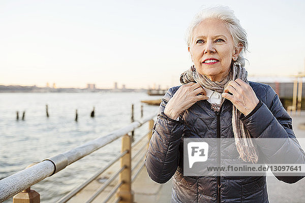 Nachdenkliche ältere Frau mit Schalldämpfer auf der Promenade bei Sonnenuntergang