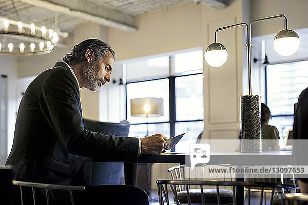 Businessman studying documents while sitting at creative office with female colleague in background