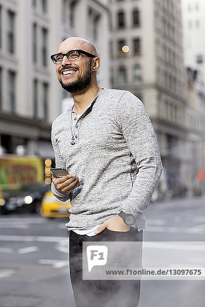Smiling man holding smart phone and standing on street
