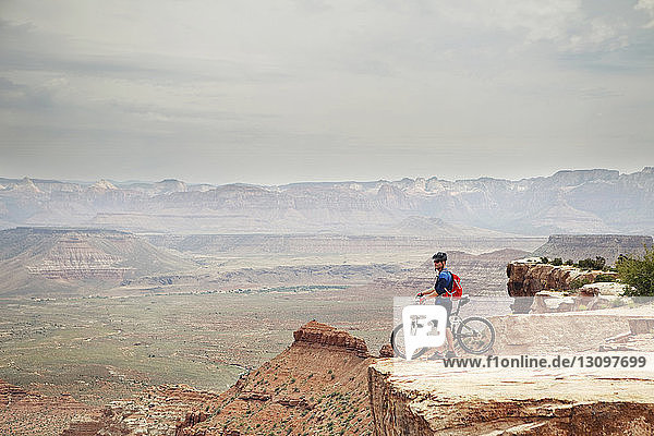 Mann steht mit Fahrrad auf Klippe gegen Berge