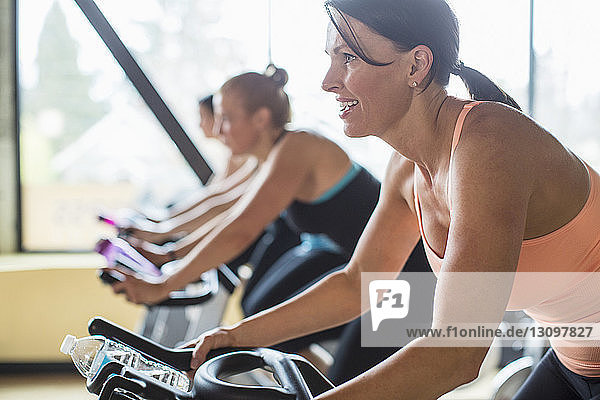 Smiling women cycling on exercise bikes at health club