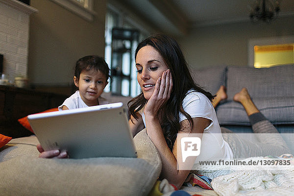 Mädchen sieht Mutter an  die zu Hause einen Tablet-Computer benutzt