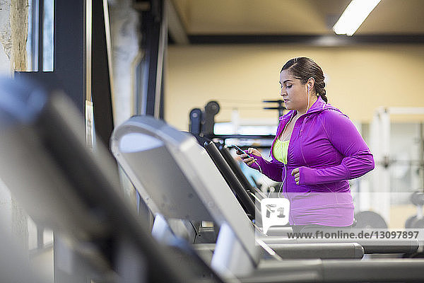 Frau benutzt Mobiltelefon beim Training auf dem Laufband im Fitnessstudio
