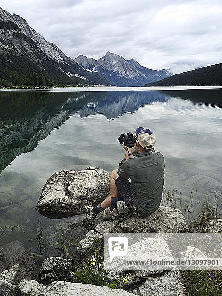 Man sitting on rock and photographing lake with camera
