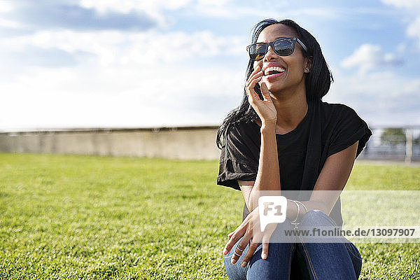 Fröhliche Frau mit Sonnenbrille auf einem Grasfeld im Park sitzend