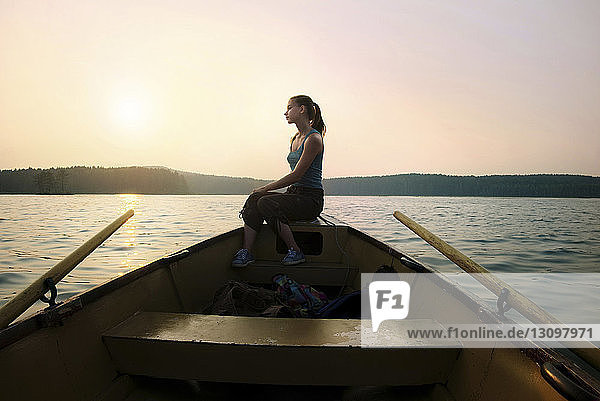 Nachdenkliche Frau sitzt am Schiffsbug im Kanu gegen klaren Himmel in der Dämmerung
