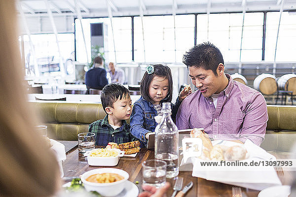Father with children using tablet computer while having lunch at restaurant