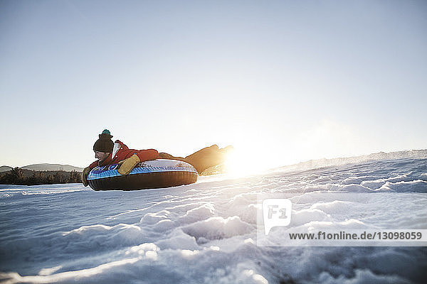Mann mit Snowtubing auf Berg gegen klaren Himmel bei Sonnenschein