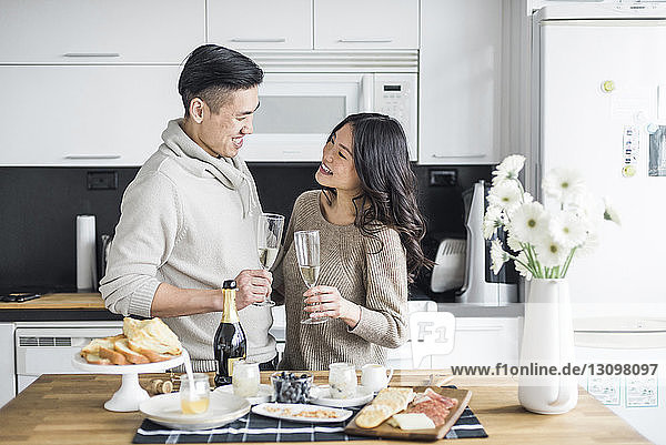 Glückliches Paar mit Getränken  das sich gegenseitig ansieht  während es zu Hause in der Küche steht