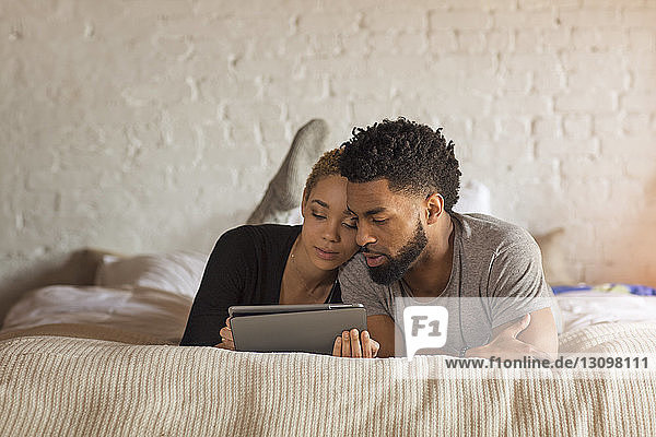 Multi-ethnisches Paar benutzt Tablet-Computer  während es zu Hause im Bett liegt