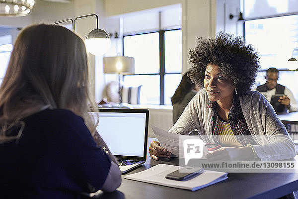 Geschäftsfrauen diskutieren über Dokumente mit Kollegen im Hintergrund im Kreativbüro