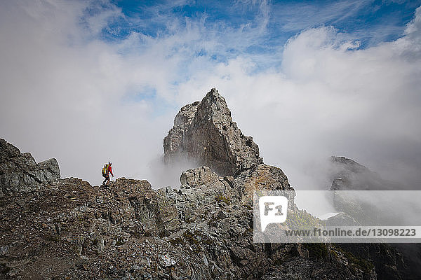 Hochwinkelaufnahme eines Wanderers mit Rucksack auf einem Berg inmitten von Wolken