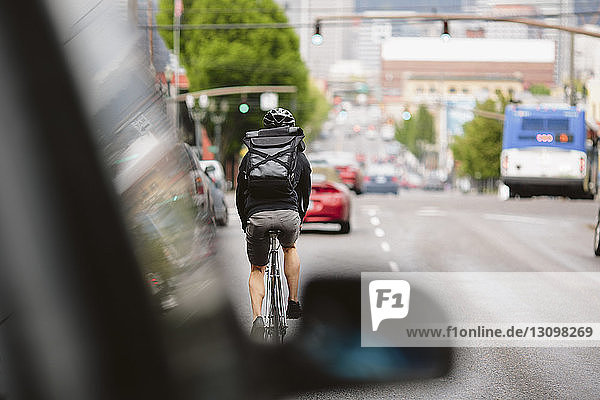 Rückansicht eines männlichen Pendlers mit Rucksack  der auf der Straße Fahrrad fährt