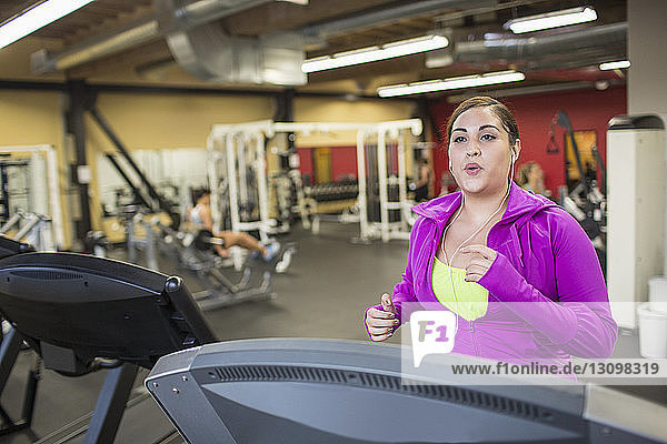 Frau hört Musik  während sie im Fitnessstudio auf dem Laufband trainiert