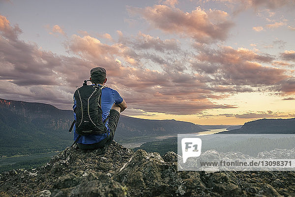 Rückansicht eines auf einem Berg sitzenden Wanderers mit Rucksack im Crater Lake National Park