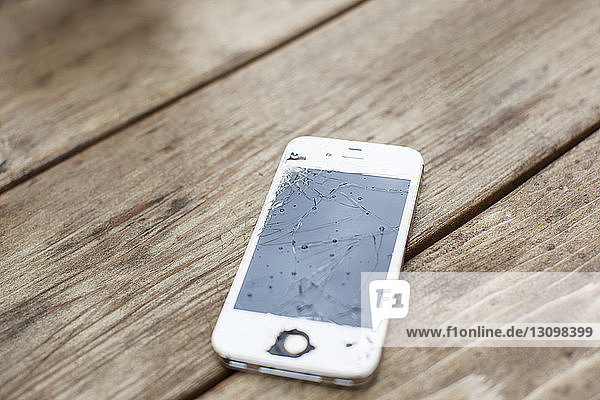 Nahaufnahme eines Smartphones mit gerissenem Bildschirm auf einem Holztisch