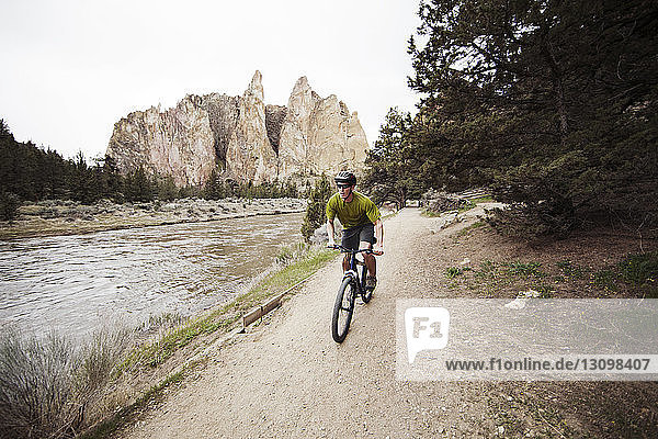 Young man riding bicycle on footpath by lake