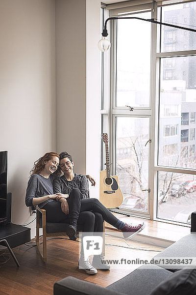 Glückliches lesbisches Paar sitzt zu Hause auf einem Stuhl am Fenster