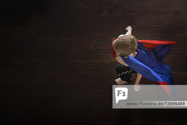 Draufsicht auf einen Jungen  der einen Superhelden-Umhang trägt  während er auf einem Hartholzboden läuft