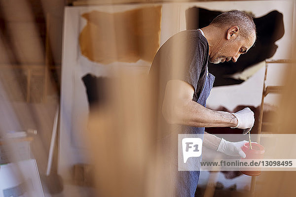 Side view of male artist mixing paint in container at workshop
