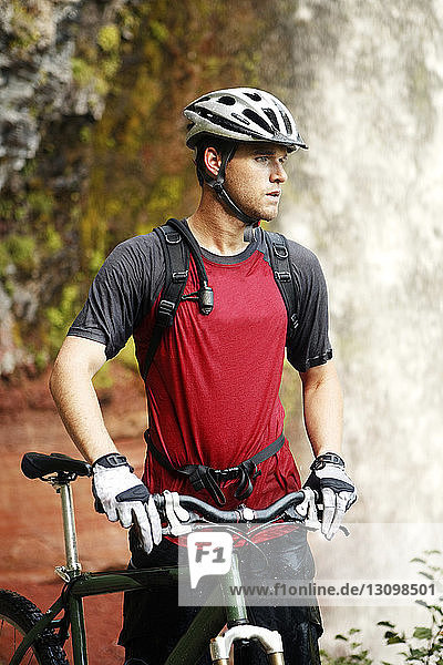 Mountain Biker holding bicycle and standing against waterfall