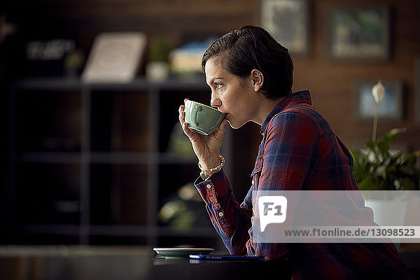 Seitenansicht einer Frau  die Kaffee trinkt  während sie im Café steht