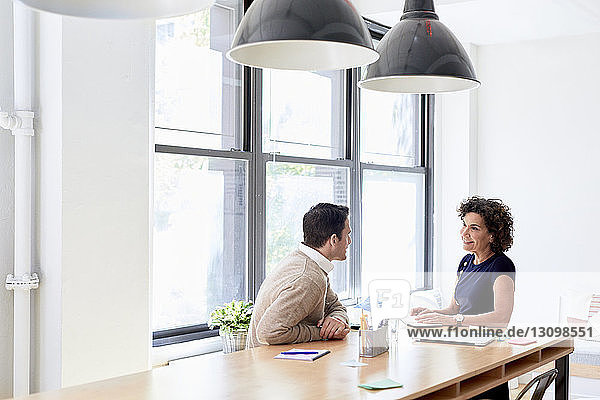 Geschäftskollegen diskutieren am Konferenztisch  während sie im Kreativbüro am Fenster sitzen