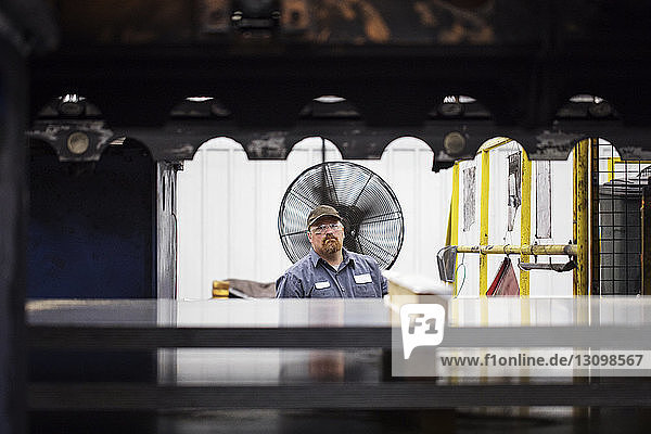 Porträt eines Arbeiters  der in einer Fabrik der Stahlindustrie gegen Bleche steht