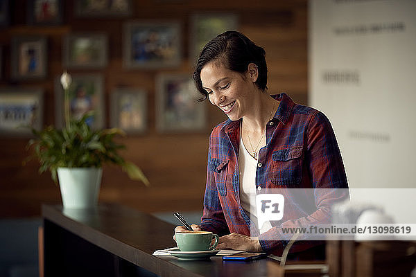 Lächelnde Frau schreibt  während sie im Cafe steht