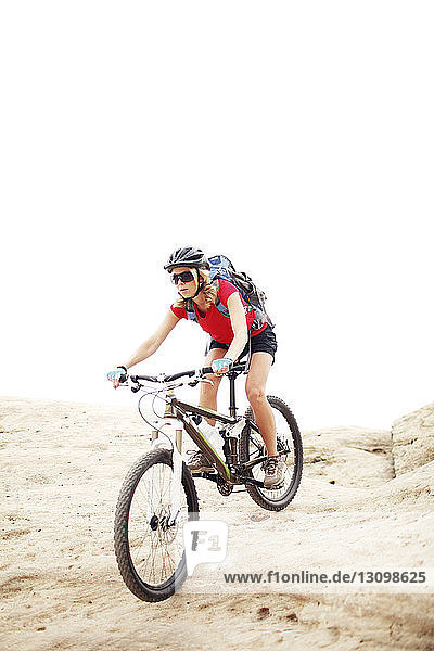 Woman riding bicycle on mountain against clear sky