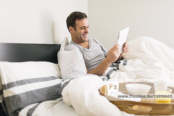 Mann benutzt Tablet-Computer  während er zu Hause am Bett sitzt