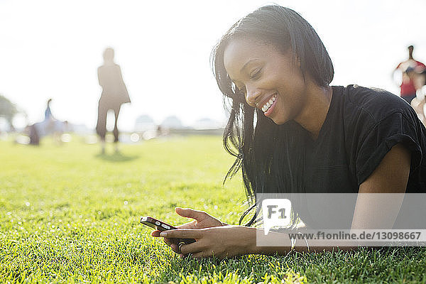 Glückliche Frau sendet Textnachrichten  während sie auf dem Feld liegt