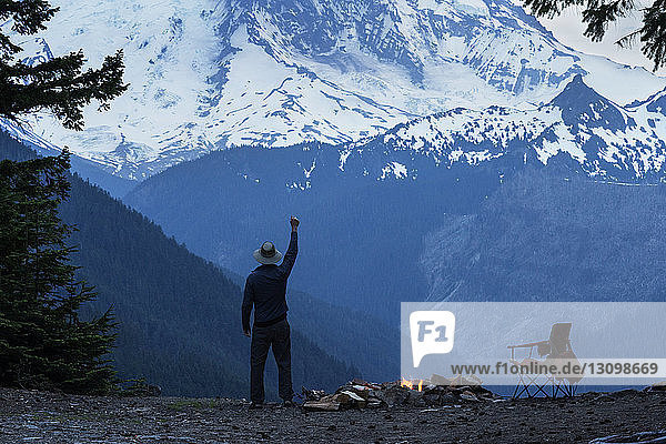 Mann mit erhobenem Arm steht gegen schneebedeckten Berg