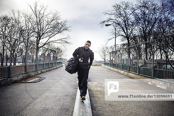 Full length of male athlete carrying bag while walking on footpath during winter